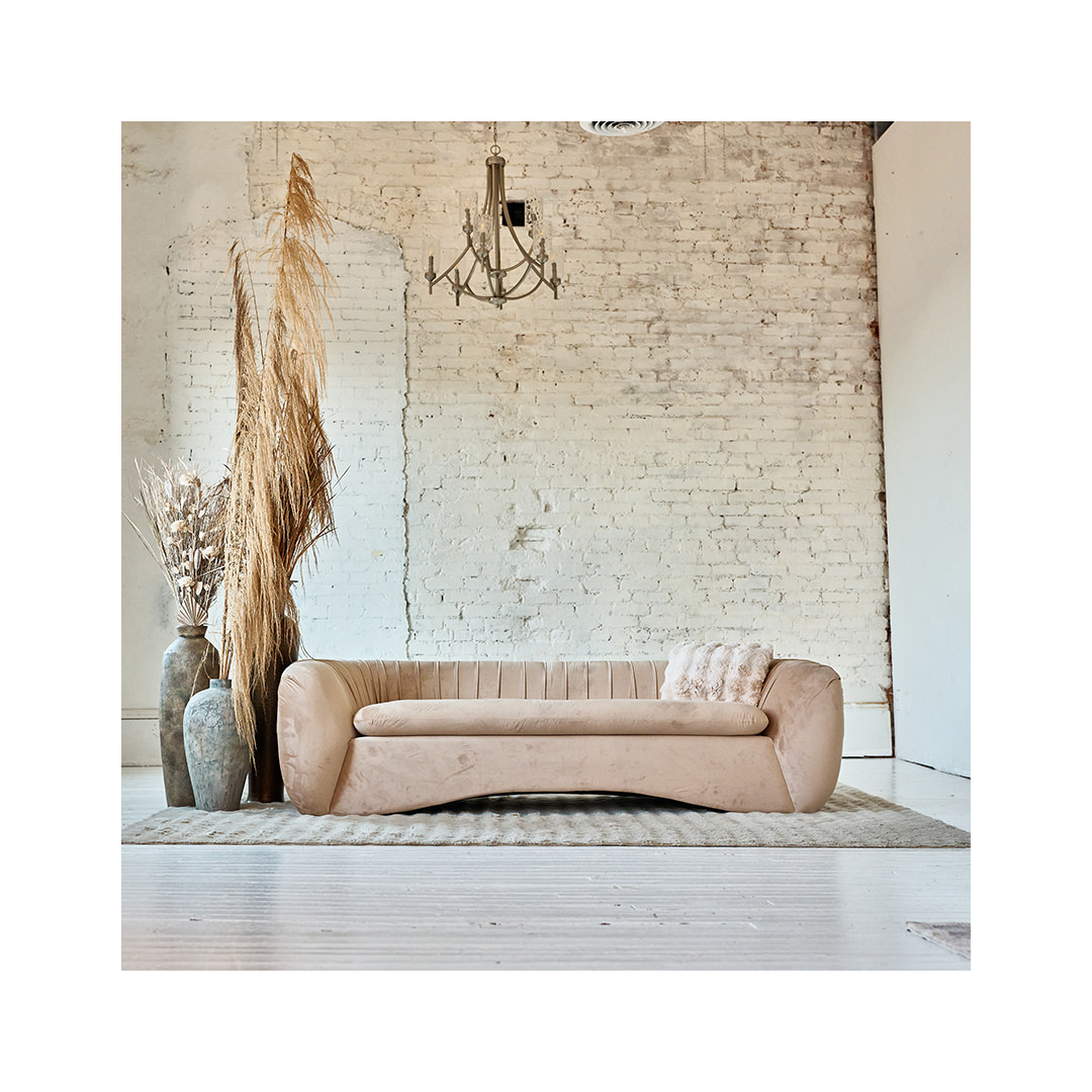 The PrivatePlay lounge: a curved blush velvet sofa and pampas grass against an exposed white-brick wall, lit by a chandelier.